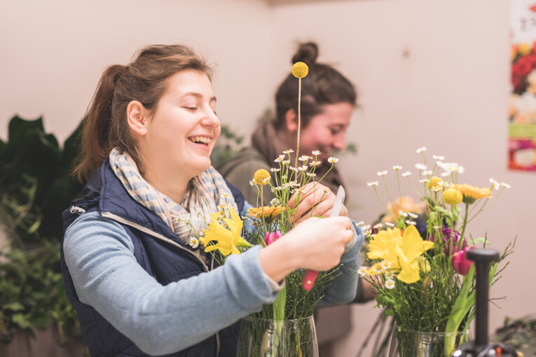 Zwei Mitarbeiterinnen stellen lachend Blumensträuße aus verschiedenen gelben Blumen zusammen