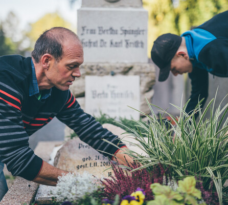 Zwei Mitarbeiter versorgen liebevoll die Pflanzen an einem Grab