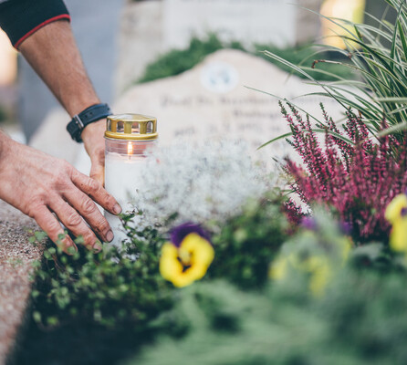 Ein Mitarbeiter platziert abschießend eine weiße Kerze auf ein mit Blumen geschmücktes Grab