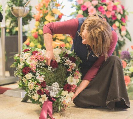 Am Boden kniende Floristin, die ein Grabgesteck in Herzform mit Blumen steckt.