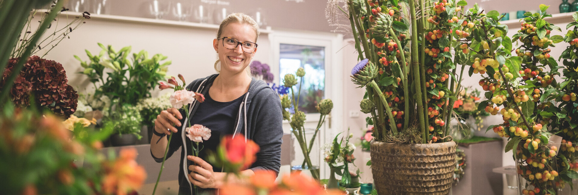 Eine junge Mitarbeiterin stellt im Laden lächelnd ein Blumenarrangement zusammen