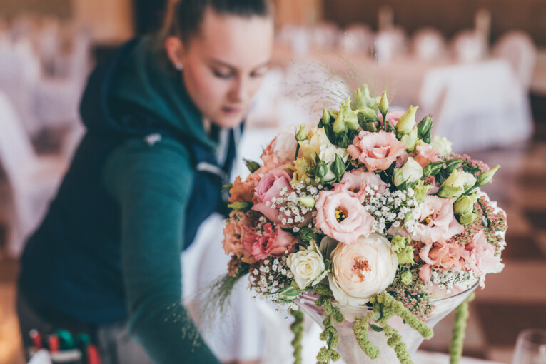 Eine Mitarbeitern platziert die liebevoll zusammengestellte Blumendekoration auf einem Tisch