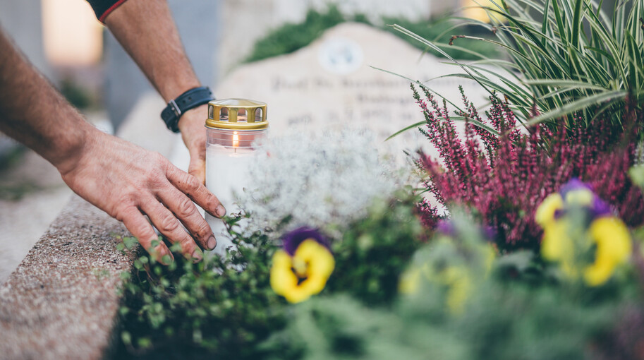 Ein Mitarbeiter platziert eine weiße Kerze auf einem mit Blumen geschmückten Grab
