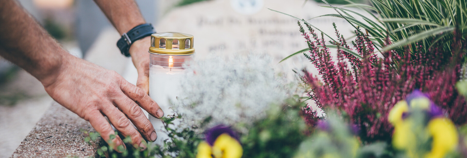 Ein Mitarbeiter stellt eine weiße Kerze auf ein mit Blumen geschmücktes Grab