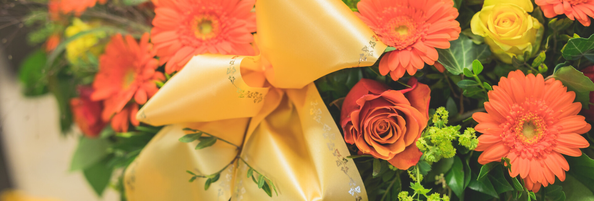 Nahaufnahme von einem Trauerkranz mit orangen und gelben Blüten und einer gelben Schleife
