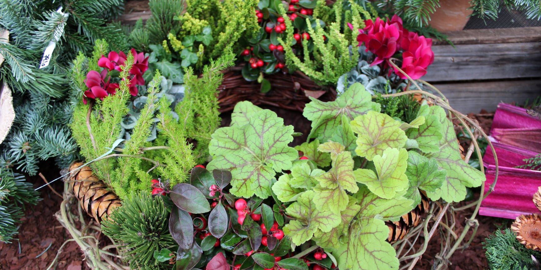 Eine liebevoll zusammengestellte Tischdekoration aus Tannenzweigen, einer weißen Kerze, einer weißen Feder, einem goldenen Herz und einer dunkelgrünen Masche auf einer Basis aus Zweigen