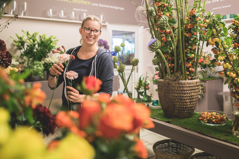 Eine Mitarbeiterin sucht lächelnd die passenden Schnittblumen für einen Strauß aus
