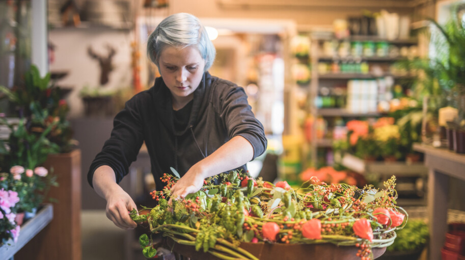 Eine Mitarbeiterin verleiht einem grün-roten Kranz den letzten Schliff