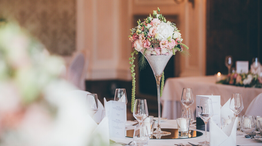 Die festlich gestalteten Tische einer Hochzeit mit pastellgrünen, weißen und pastellrosa Blumendekoration