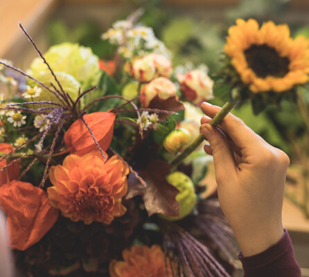 Eine Mitarbeiterin steckt eine Sonnenblume in einen liebevoll zusammengestellten Strauß