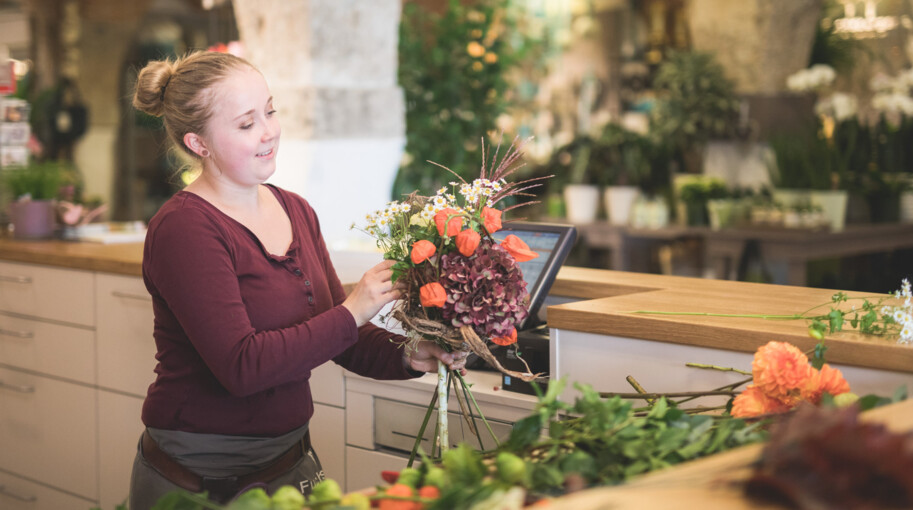 Eine Mitarbeiterin stellt im Blumengeschäft einen detailverliebten Strauß zusammen
